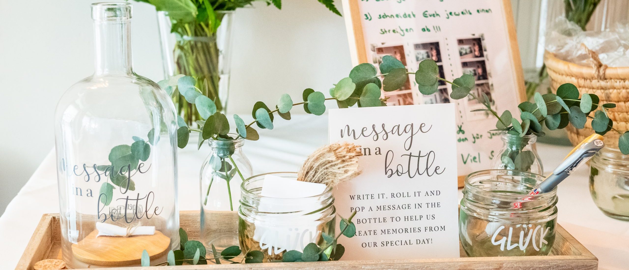 Ein Tisch mit einem Hochzeitsgästebuch in Form von einer Flasche, mit kleinen Papierröllchen auf die man Grüße an das Brautpaar schreibt. Aufgestellt bei einer Hochzeit im Luca Steakhaus in Bedburg.
